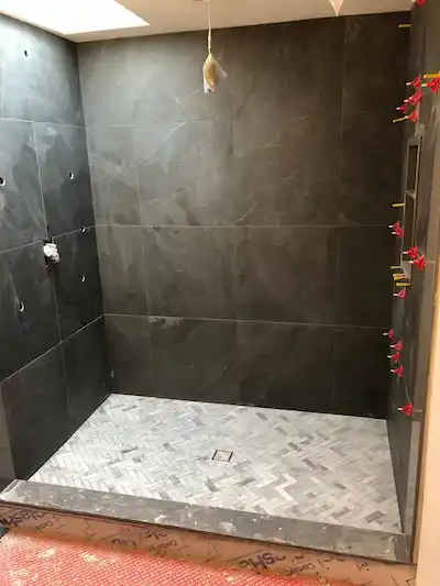 Walk-in shower renovation featuring dark grey wall tiles and light grey marble herringbone floor tiling