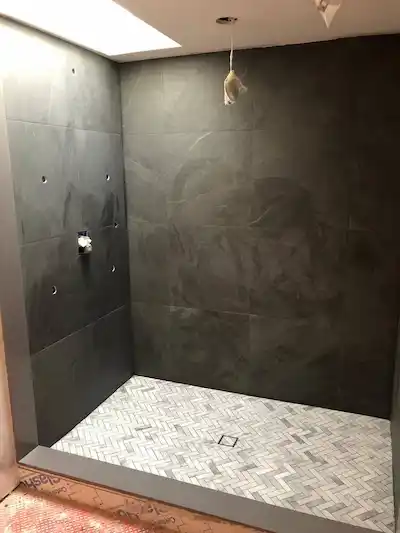 Luxury shower stall construction with charcoal stone-look tiles and marble herringbone mosaic floor