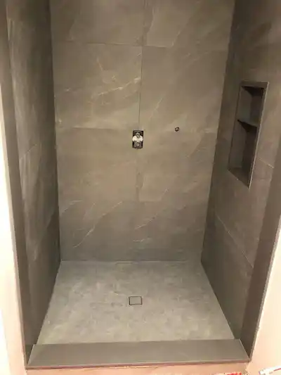 Completed custom shower interior with large-format taupe stone walls and built-in recessed niche