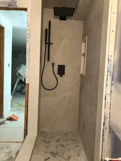 Modern minimalist shower design with light beige tiles, marble herringbone floor, and matte black fixtures