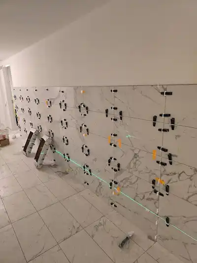 Precision installation of large marble-veined porcelain wall tiles using professional laser leveling